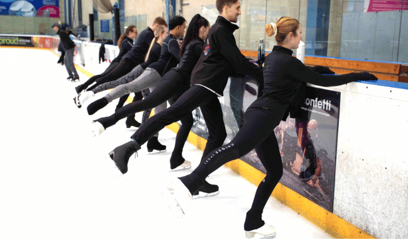 Photo of ice skating lessons. You can see several adults lined up in a row, holding onto the side of the barrier